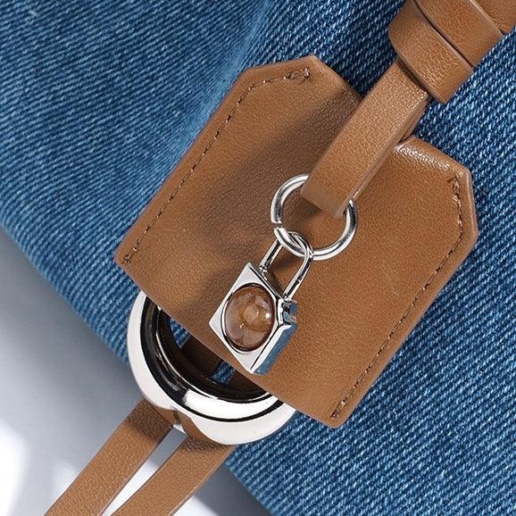 Denim bag with brown leather strap, silver ring, and small decorative lock detail