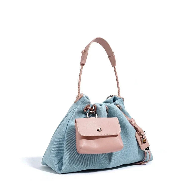 Blue denim handbag with pink leather handle and attached mini pouch, white background