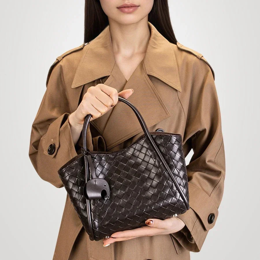 Woman in tan trench coat holding black woven leather handbag