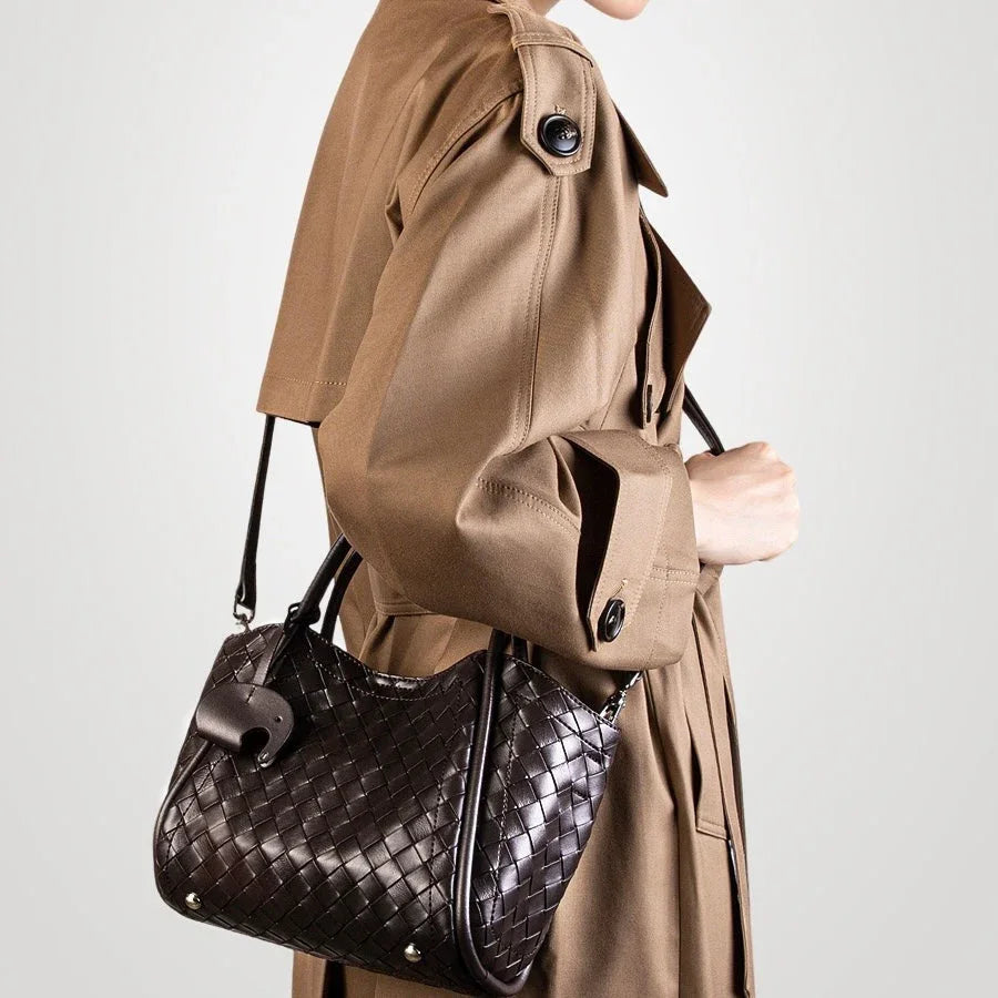 Woman in tan trench coat carrying black woven leather shoulder bag