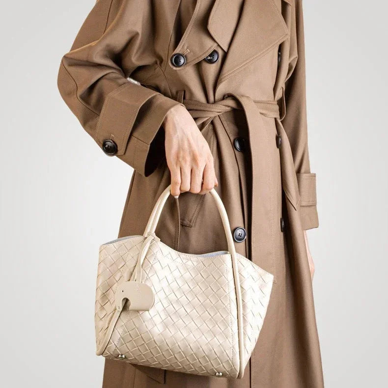 Woman in brown trench coat holding woven beige leather handbag