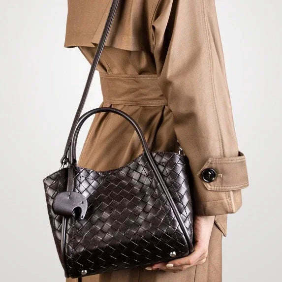 Woman in beige trench coat holding black woven leather handbag with shoulder strap