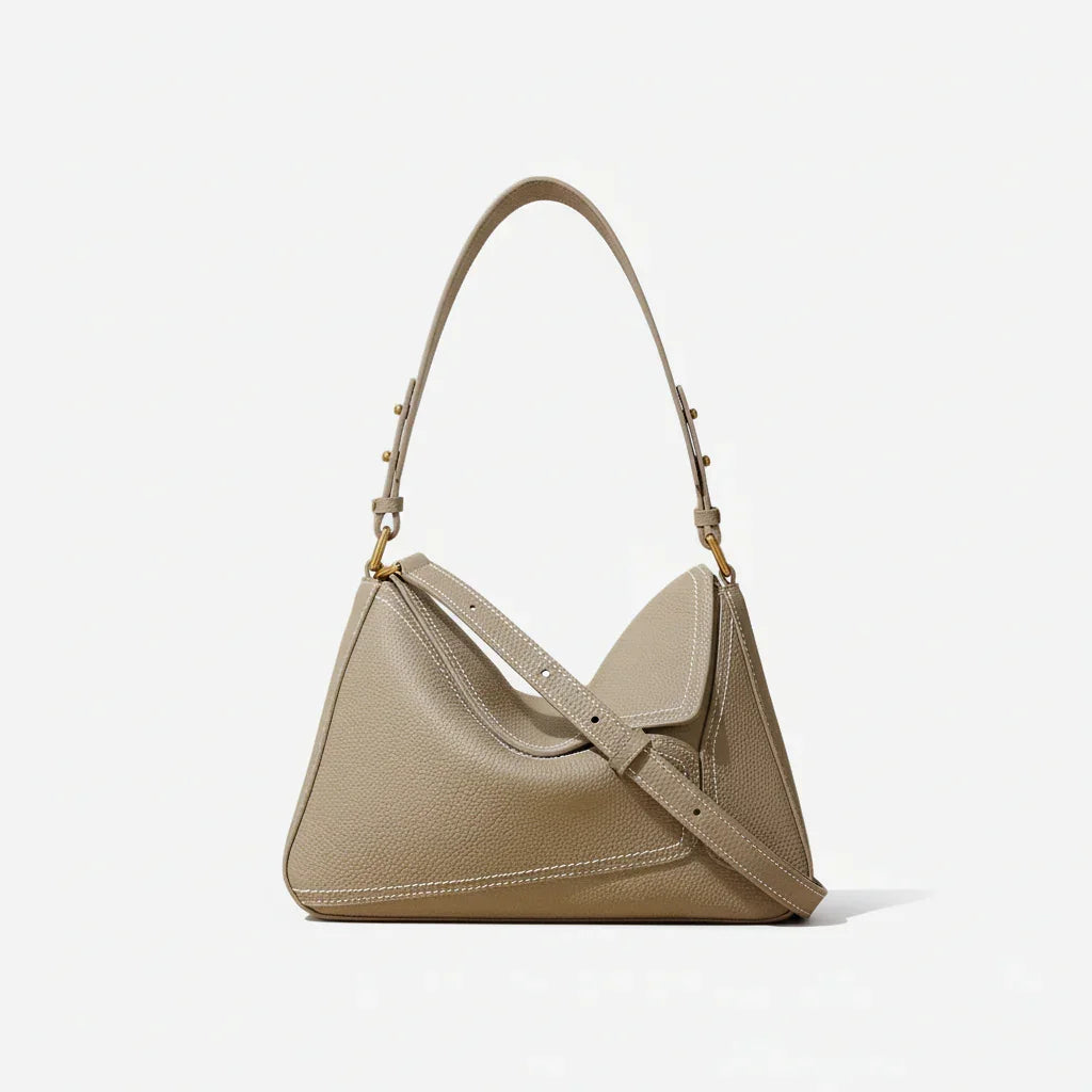 Taupe leather shoulder bag with gold hardware and top handle on neutral background