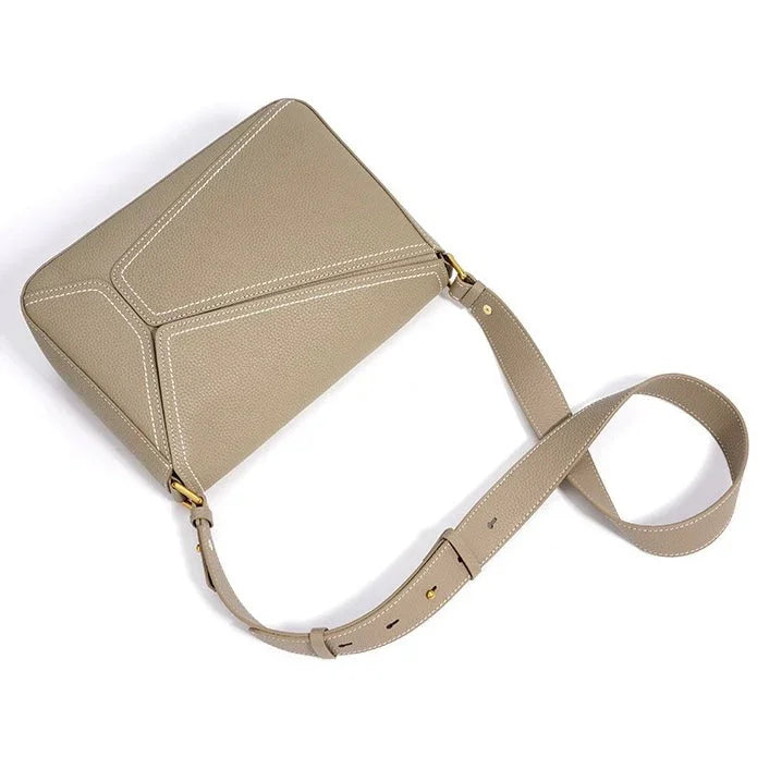 Taupe leather crossbody bag with white stitching and adjustable strap on white background