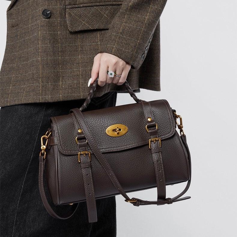 Woman holding a dark brown leather satchel handbag with gold hardware