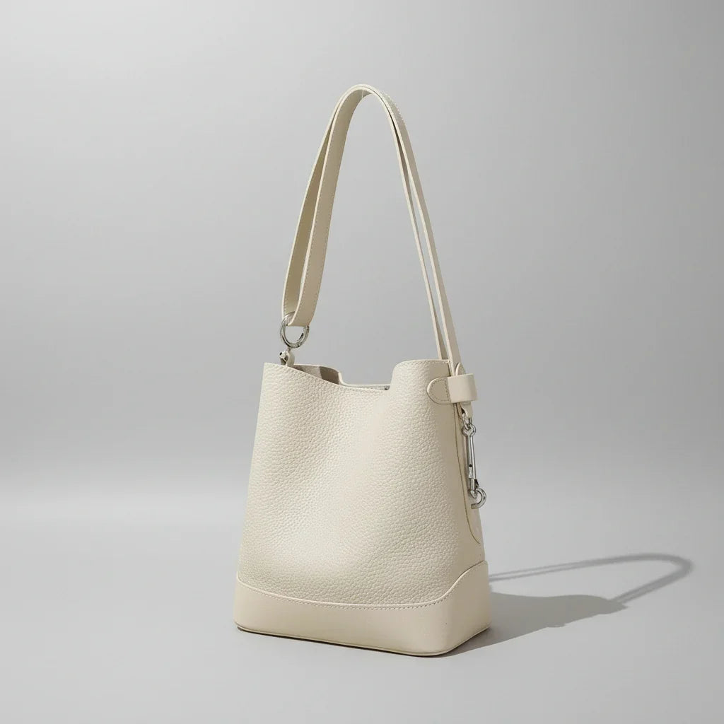 Minimalist cream leather bucket bag with shoulder strap in soft natural lighting