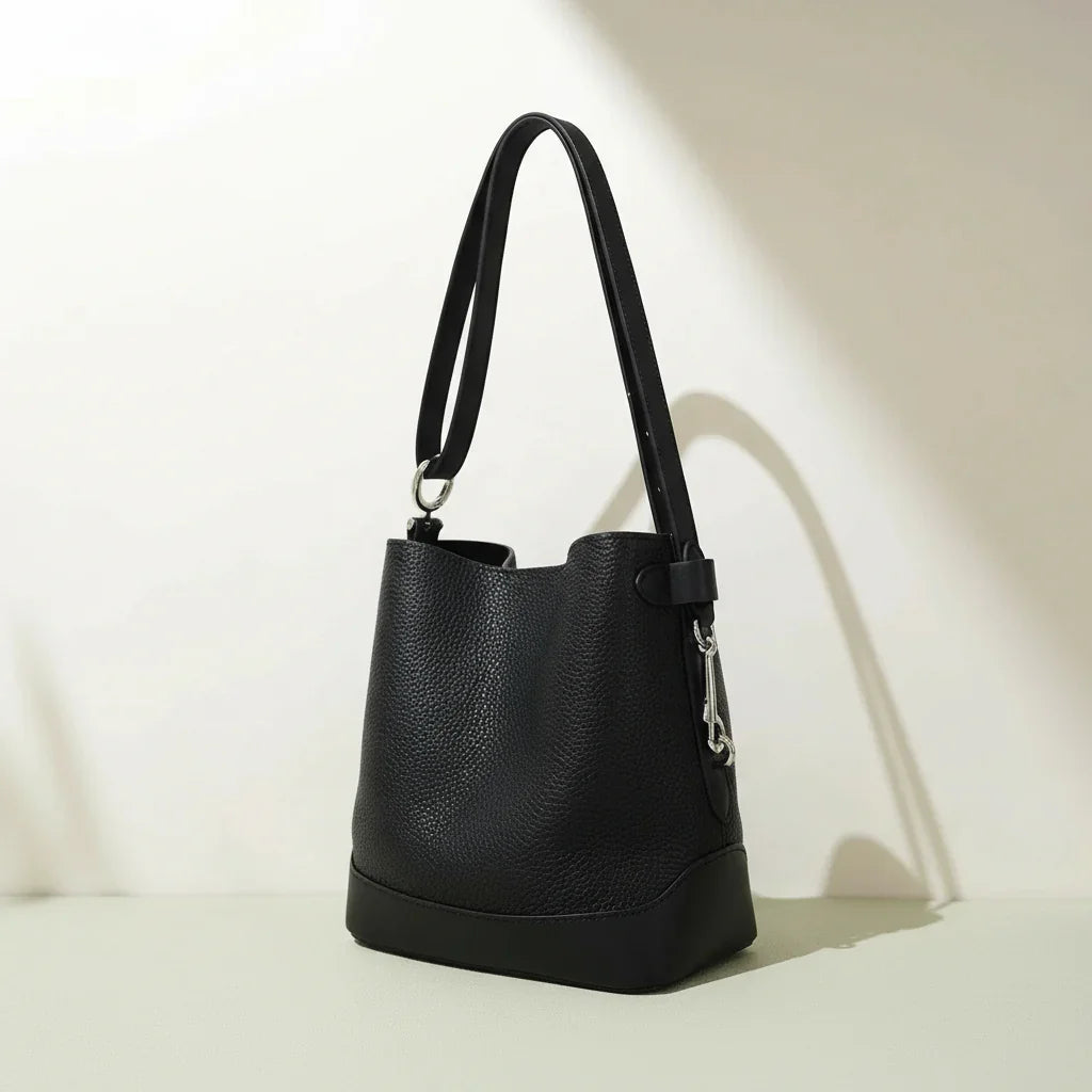 Black leather bucket bag with shoulder strap on light surface, minimalist background