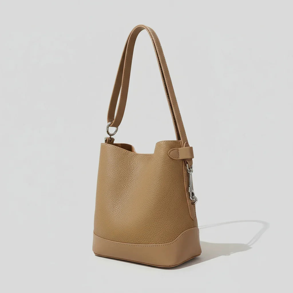 Tan leather bucket bag with shoulder strap on light background, minimalist fashion accessory