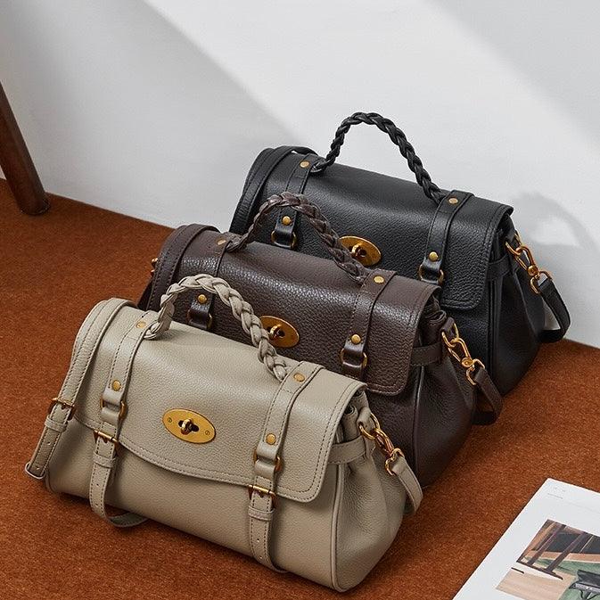 Three leather satchel handbags in beige, brown, and black with gold hardware on a brown surface