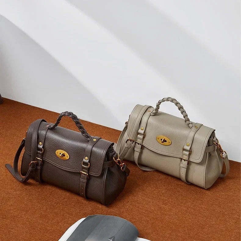 Two leather satchel handbags with braided handles on a brown surface