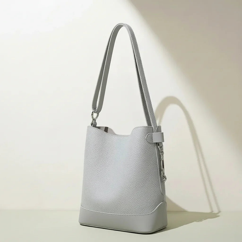 Minimalist light grey leather bucket bag with shoulder strap on neutral background