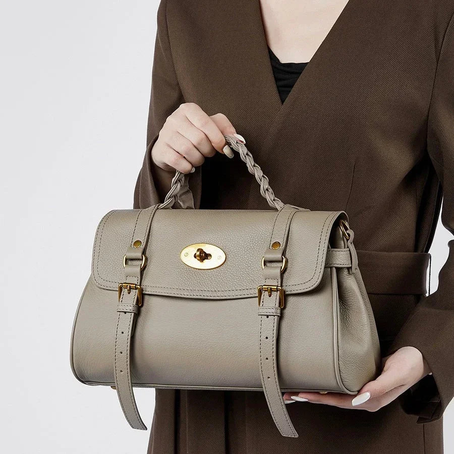 Woman in brown blazer holding taupe leather handbag with gold hardware and braided handle