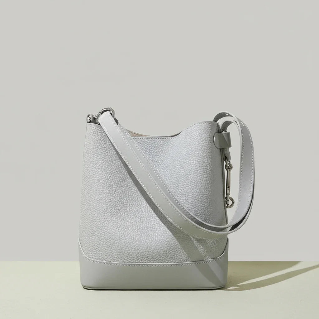Light grey leather bucket bag with wide strap on neutral background
