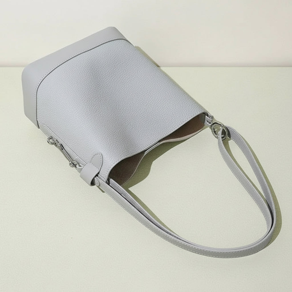 Light grey leather bucket bag with double straps on a beige surface