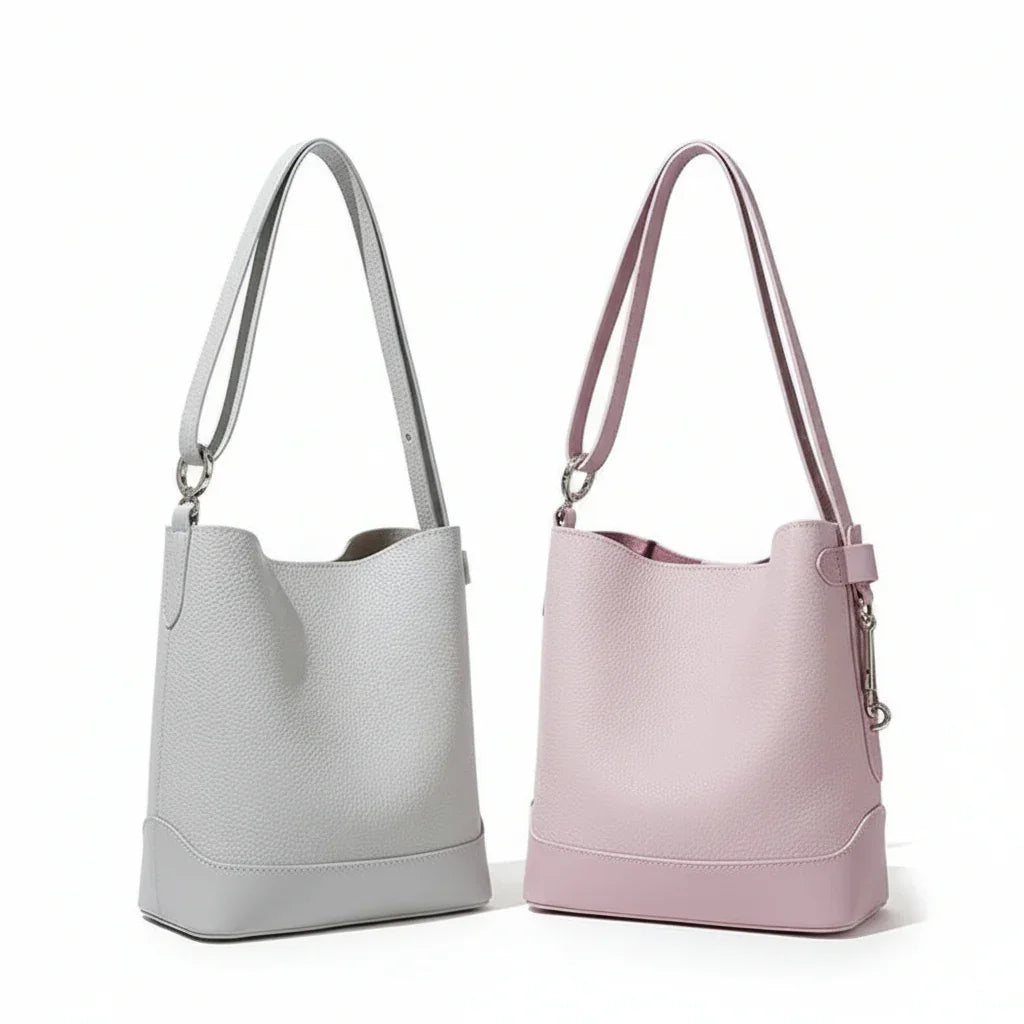 Light grey and pastel pink leather bucket bags with long straps on a neutral background
