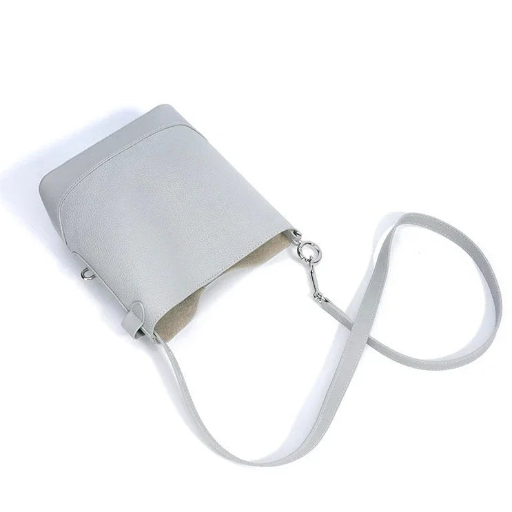 Minimalist light gray leather crossbody bag with long strap on white background