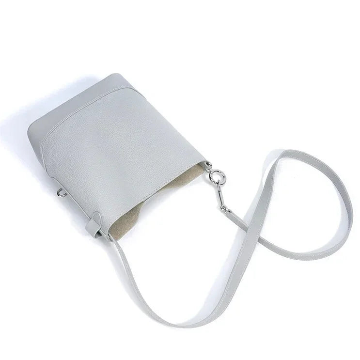 Minimalist light gray leather crossbody bag with long strap on white background