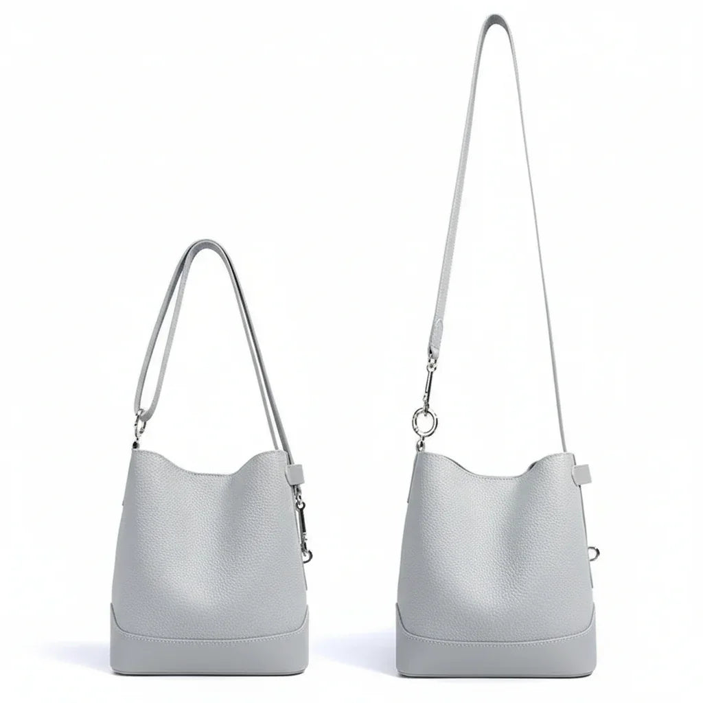 Light gray leather bucket bag with two adjustable shoulder straps on white background