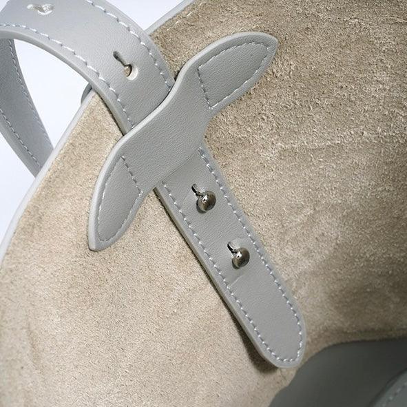 Close-up of beige suede shoe with light gray leather strap and stitched details