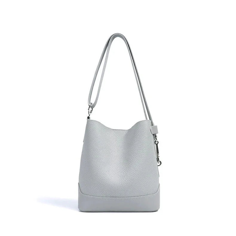 Light grey leather bucket bag with long shoulder strap on white background