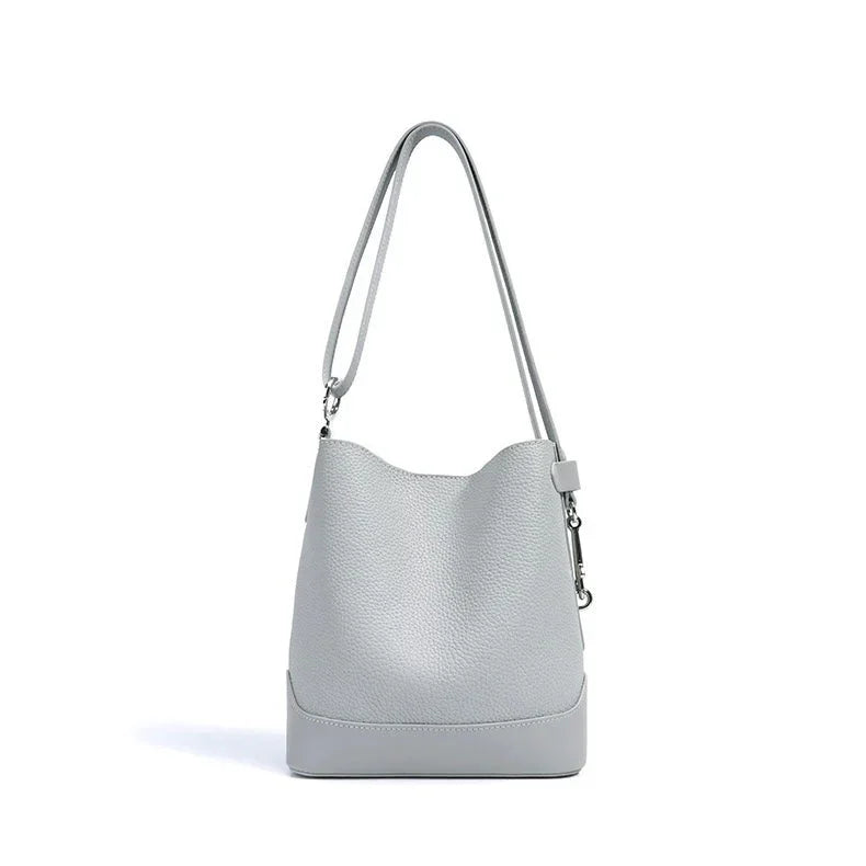 Light grey leather bucket bag with long shoulder strap on white background