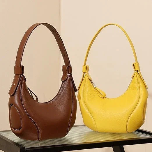 Brown and yellow leather shoulder bags on a black table against a beige wall