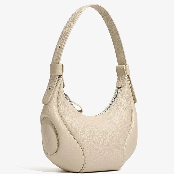 Beige crescent-shaped leather shoulder bag with zipper and textured finish on white background
