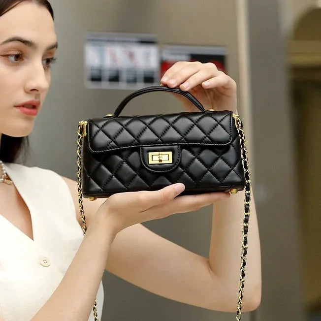 Woman holding a black quilted leather handbag with gold chain strap and clasp