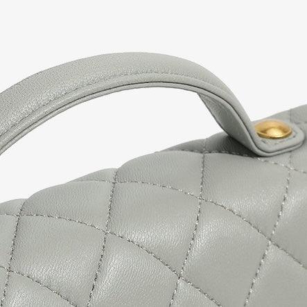 Light gray quilted leather handbag handle with gold hardware on white background