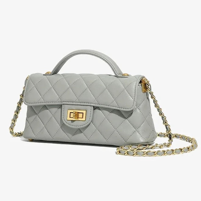 Quilted light gray leather handbag with gold chain strap and turn-lock clasp on white background.