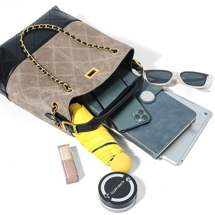 Beige and black quilted handbag with chain strap, yellow umbrella, smartphone, sunglasses, tablet, lipstick, and round cosmetic jar on white background