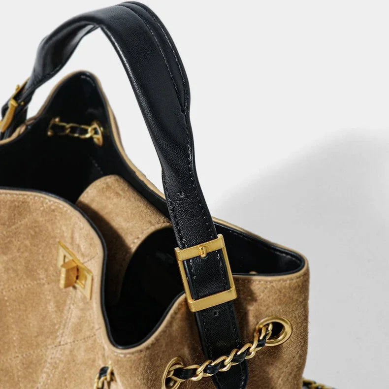 Tan suede handbag with black leather strap and gold chain hardware on white background