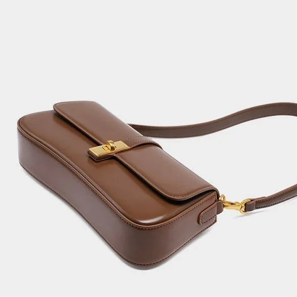Brown leather shoulder bag with gold clasp and strap on plain background