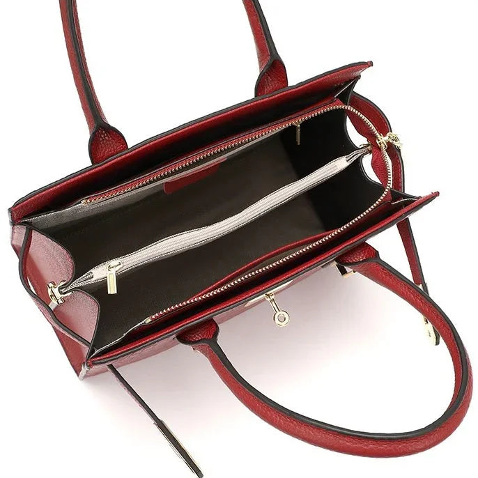 Open red leather handbag with dual handles, spacious compartments, and gold zippers