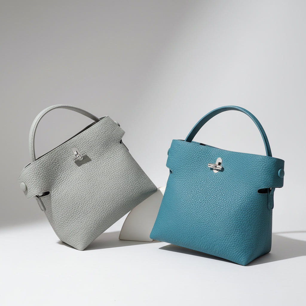 Two textured leather handbags, one gray and one teal, displayed on a beige surface