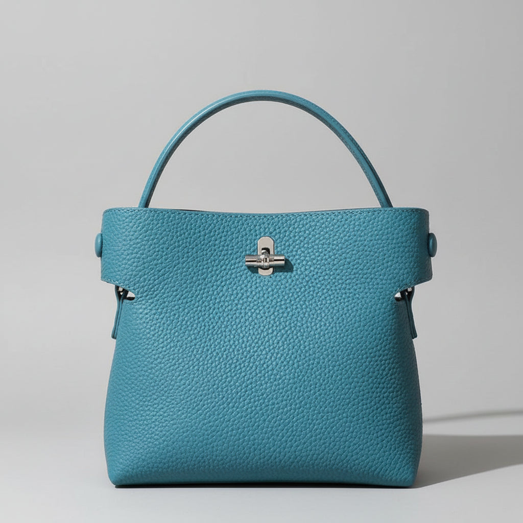Blue pebbled leather handbag with top handle and silver clasp on light background