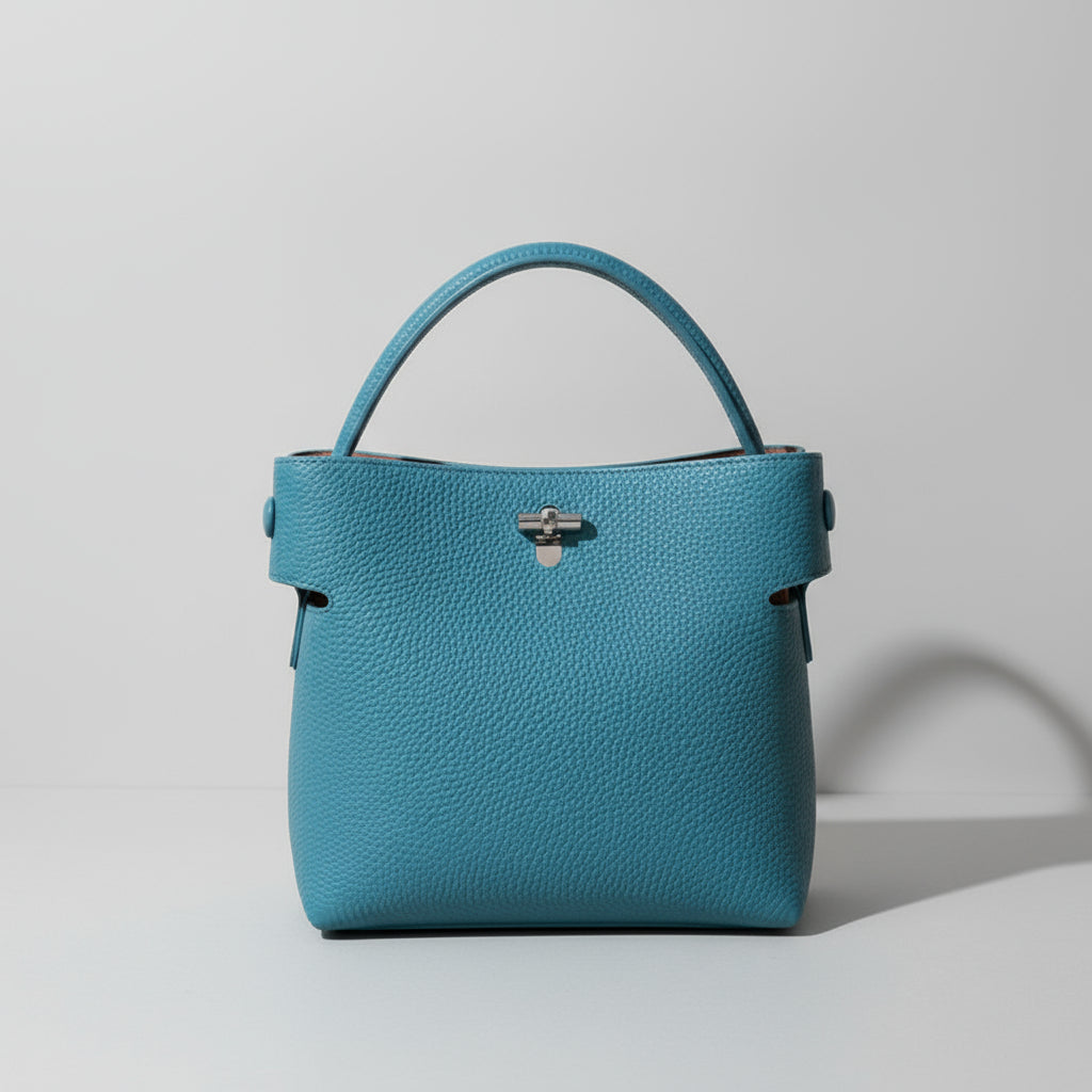 Teal leather handbag with single handle on beige surface, minimalistic style