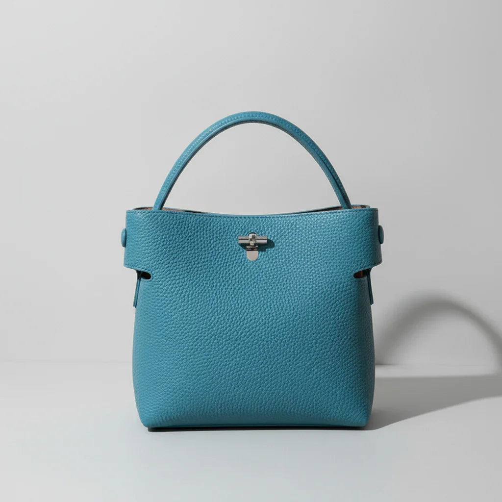 Teal leather handbag with single handle on beige surface, minimalistic style