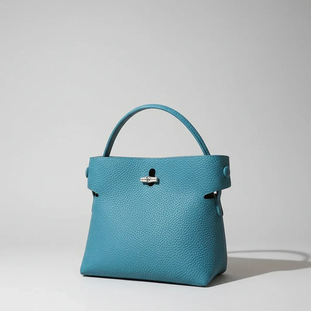 Blue leather handbag with top handle on neutral background