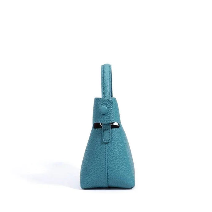 Side view of teal leather handbag with handle on white background