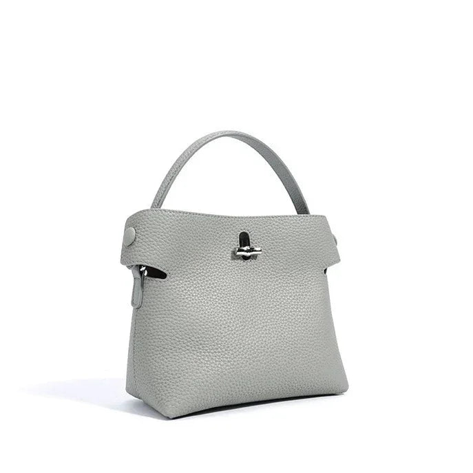 Light grey leather handbag with top handle and silver clasp on white background