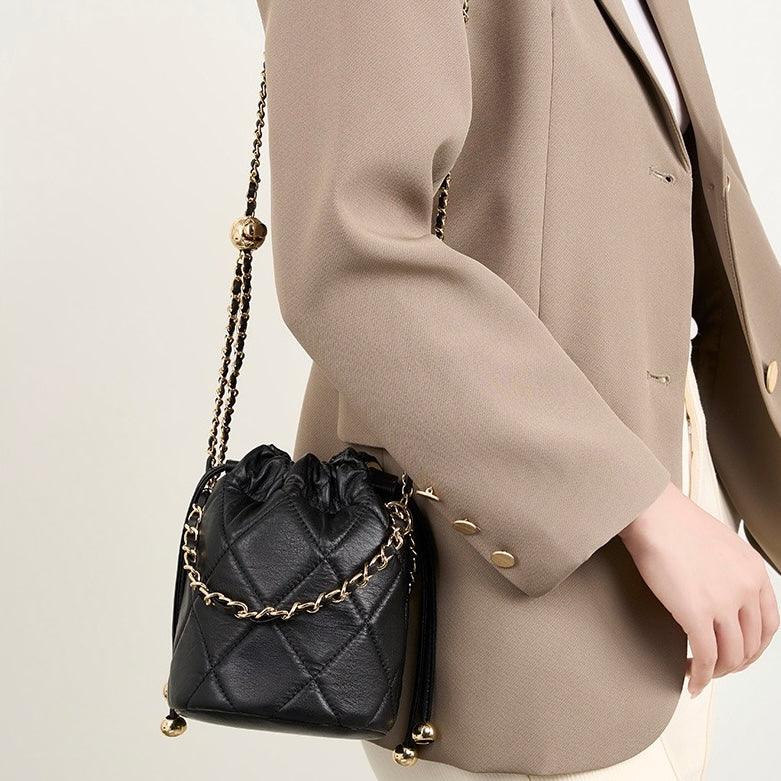 Woman in beige blazer with black quilted leather bucket bag and gold chain strap