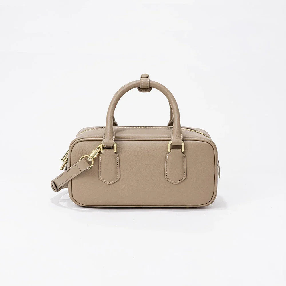 Beige leather handbag with gold hardware and top handle on white background
