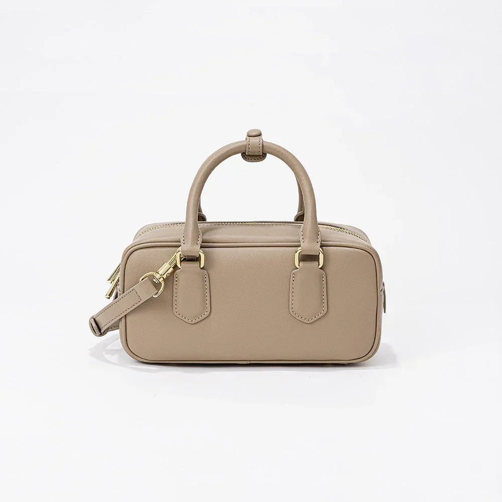 Beige leather handbag with gold hardware and top handle on white background