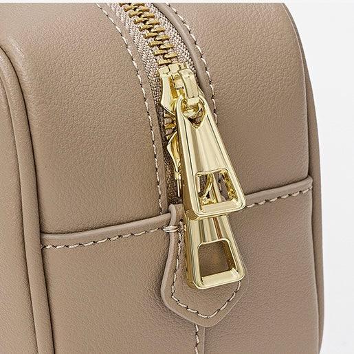 Taupe leather handbag with gold zipper pulls and detailed stitching closeup