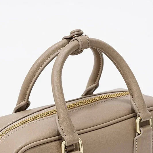 Beige leather handbag with gold zipper and double handles on white background