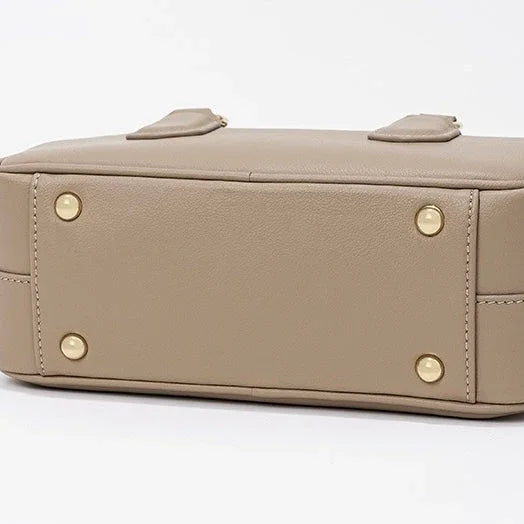 Beige leather handbag bottom with gold metal feet on white background