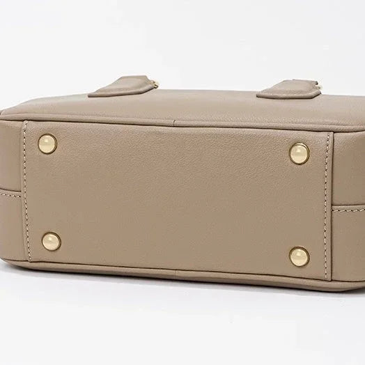 Beige leather handbag bottom with gold metal feet on white background