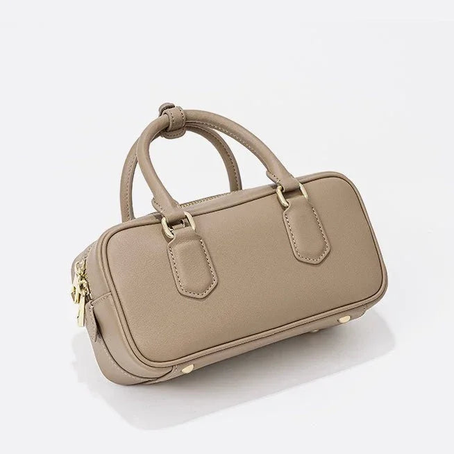 Taupe leather handbag with gold hardware and double handles on a white background