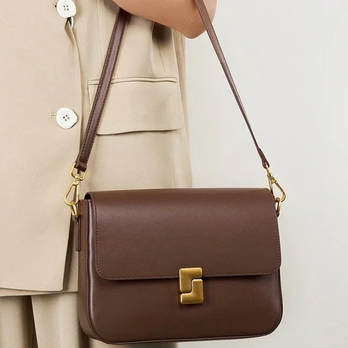 Brown leather shoulder bag with gold clasp, worn over beige blazer